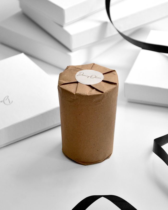 Scented candle wrapped in craft paper placed on table with heap of white boxes and black ribbon in modern studio